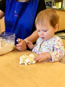 Toddler and teacher making pizza dough together