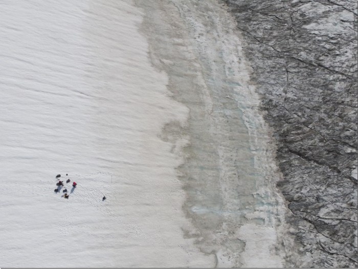 This photo shows the change in surface darkness as the cold dry white snow (left side of of image) starts melting to grey (centre of the image), to reveal the dark ice underneath (right side of image). The dots on the left are people to give a sense of the scale. Credit Laura Halbach