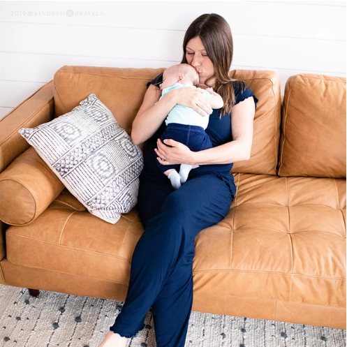 new mom on couch in nursing pajamas kissing newborn on the head