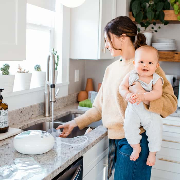 woman washing breast pump covered by insurance holding baby
